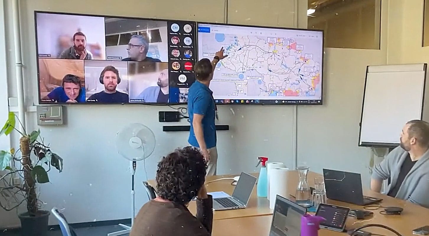 A group of diverse individuals in a meeting room, concentrating on a large screen featuring a map.